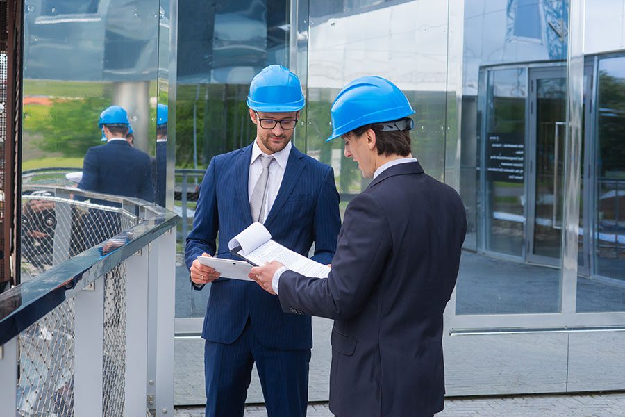 Specialized Business Insurance - Two Real Estate Developers Wearing Blue Hard Hats are Standing Together Reviewing Some Documents